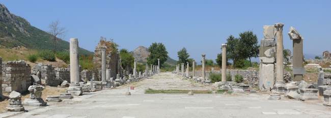 Colonnaded marble street at Ephesus lined with broken columns, leading toward rocky wooded hills