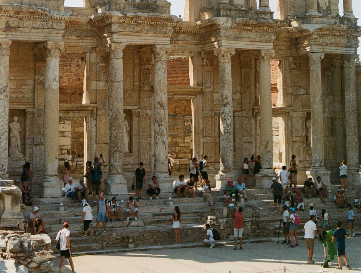 Visitors sitting on the marble steps in front of the two-story columned facade of the Library of Celsus at Ephesus