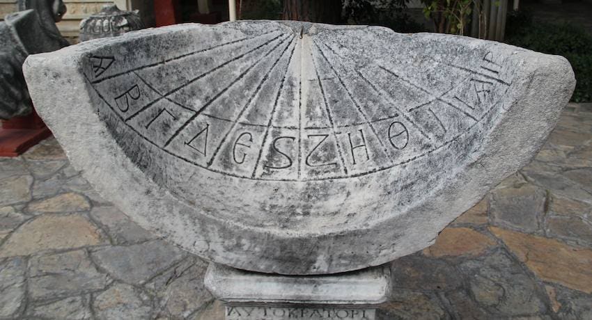 Semicircular ancient marble sundial carved with Greek letters and hour lines on a stone plinth