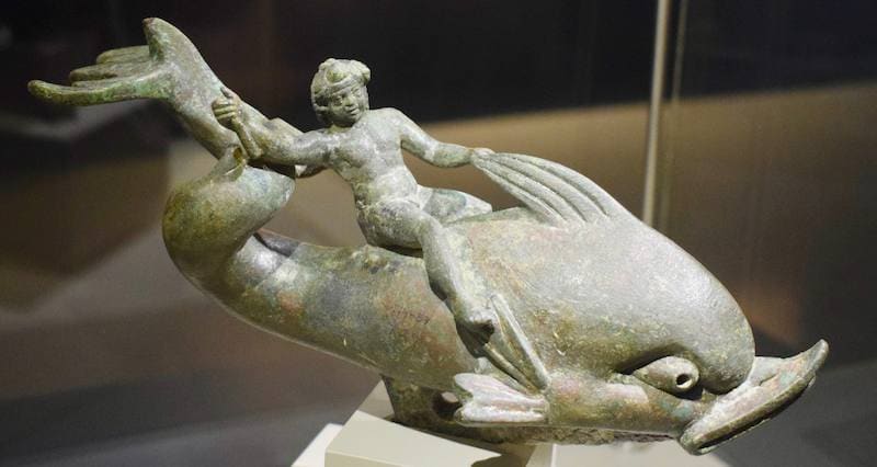 Bronze statuette of a small figure riding a dolphin, displayed in a case at the Ephesus Archaeological Museum