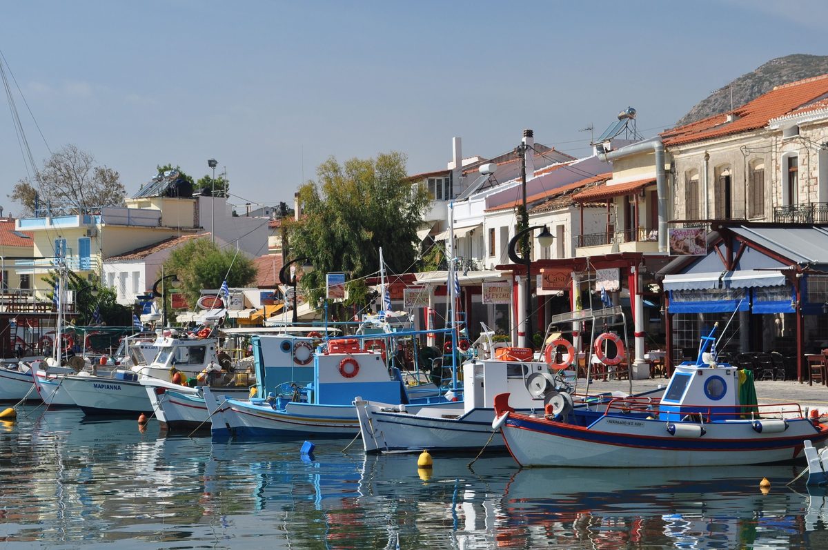 Painted wooden fishing boats moored along the harbor quay of Pythagorion on Samos, with tavernas and red-tiled houses behind