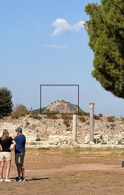 The Hill of Astyages at the western edge of ancient Ephesus, its old wall tower boxed in black, behind a line of ruined walls with two columns and a couple standing in the foreground